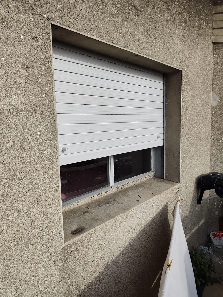 Cortina de enrollar blanca completamente abierta sobre ventana empotrada en pared simil piedra beige